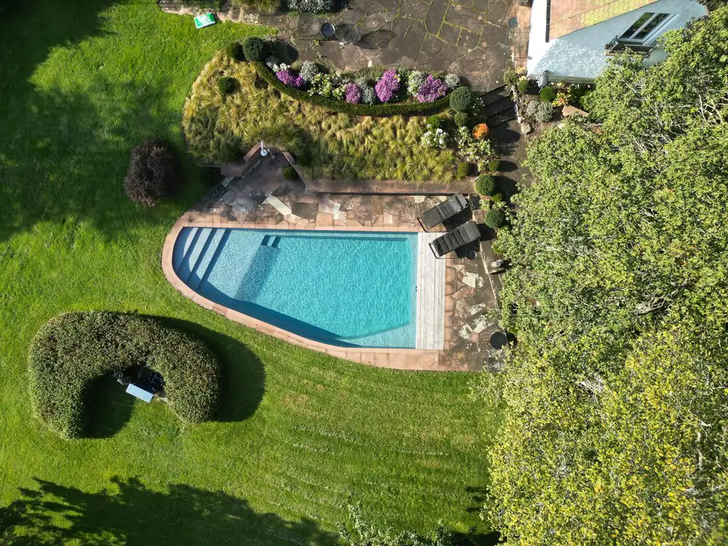 Luftaufnahme eines Pools in gestaltetem Garten mit Rasen und Hecke
