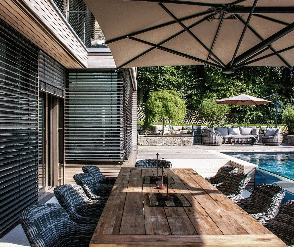 Esstisch unter dem Sonnenschirm am Pool, daneben das Haus mit Raffstores in Villingen-Schwenningen