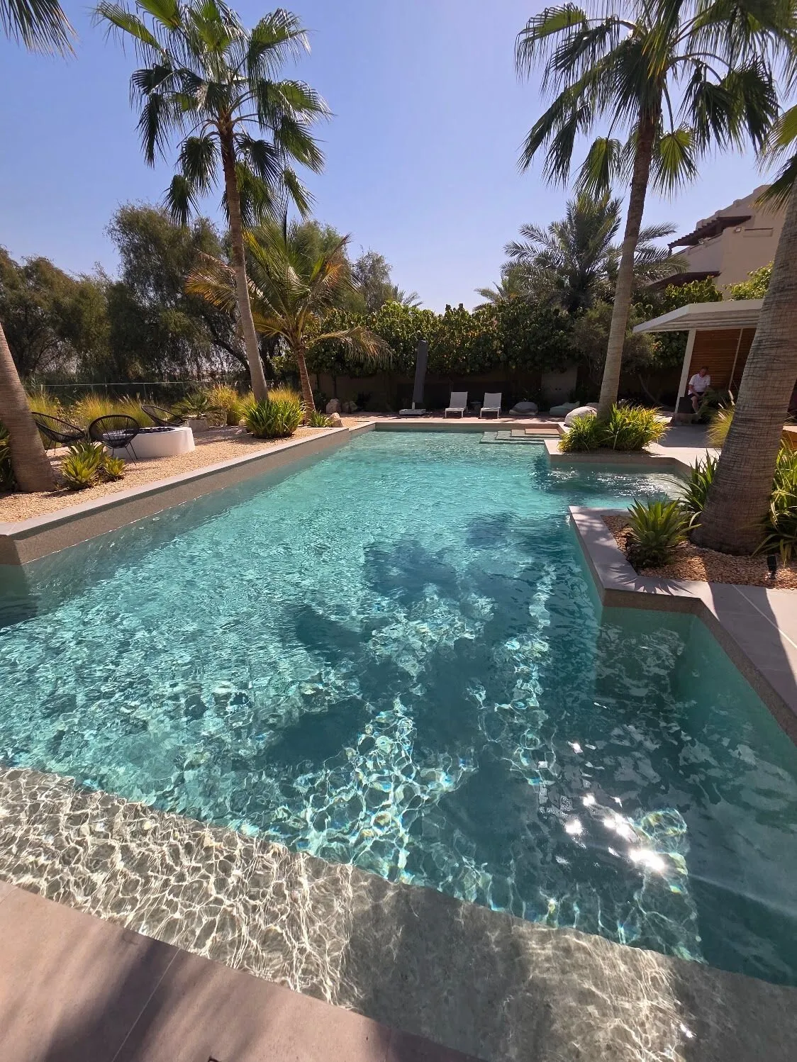 Resort-Pool unter Palmen mit Sitzstufe und flachem Einstieg im Sonnenlicht in Dubai